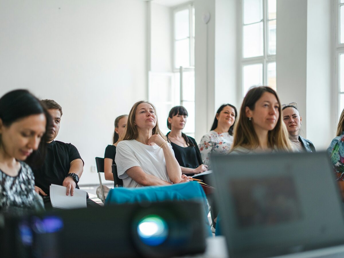 Participants seated in a bright, sunlit workshop room, listening and taking notes